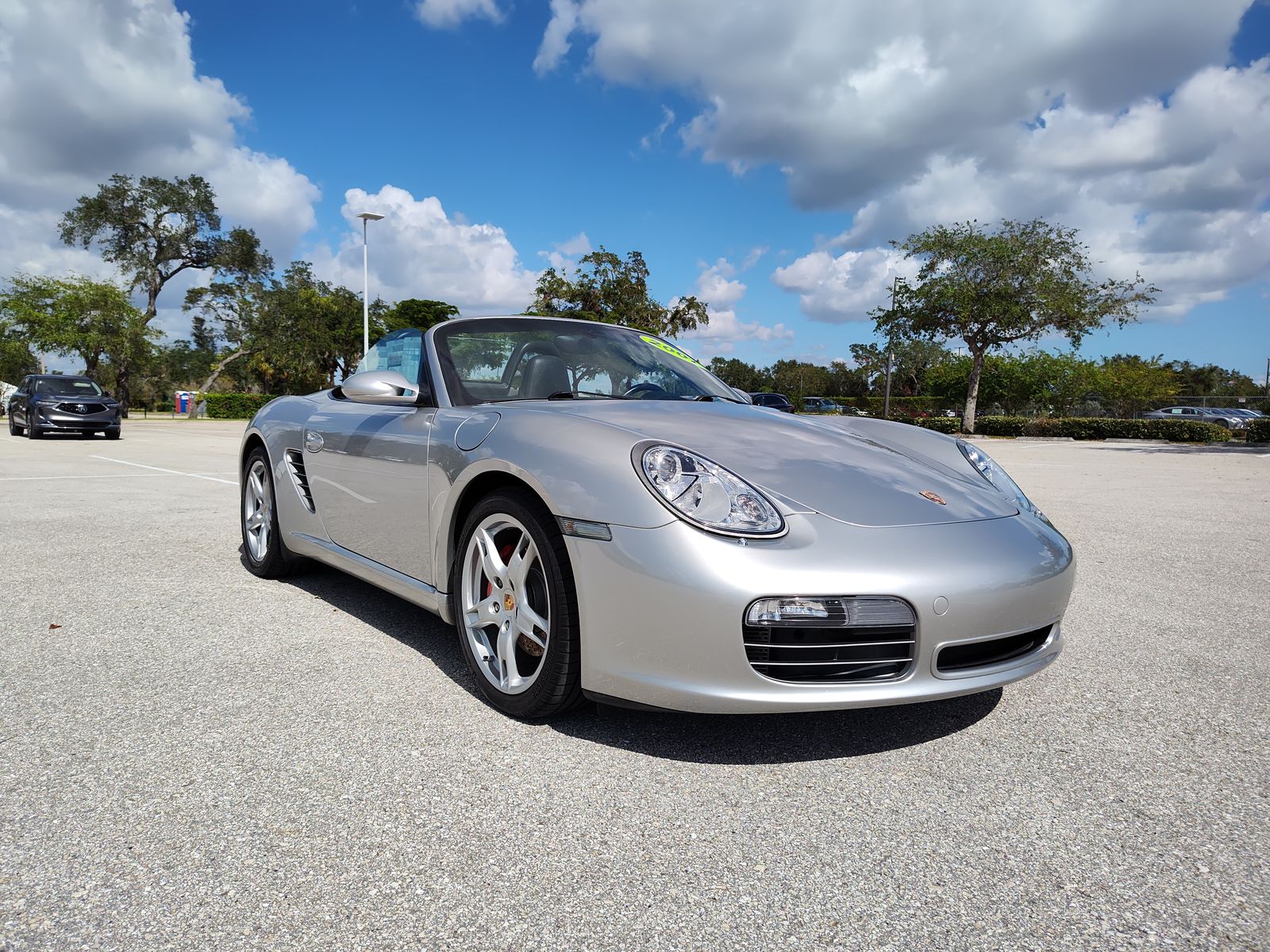 Front three-quarter of a silver Porsche Boxster convertible on a dealership lot.